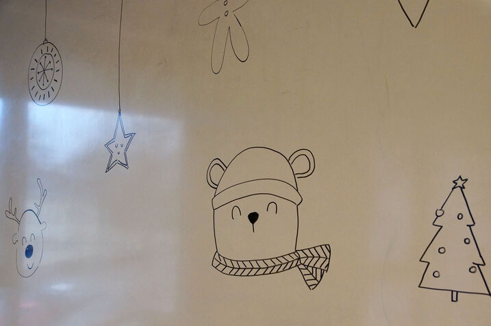 Weihnachtsmotive auf ein Whiteboard gezeichnet. Im Vordergrund ein Bär mit Haube und Schal.