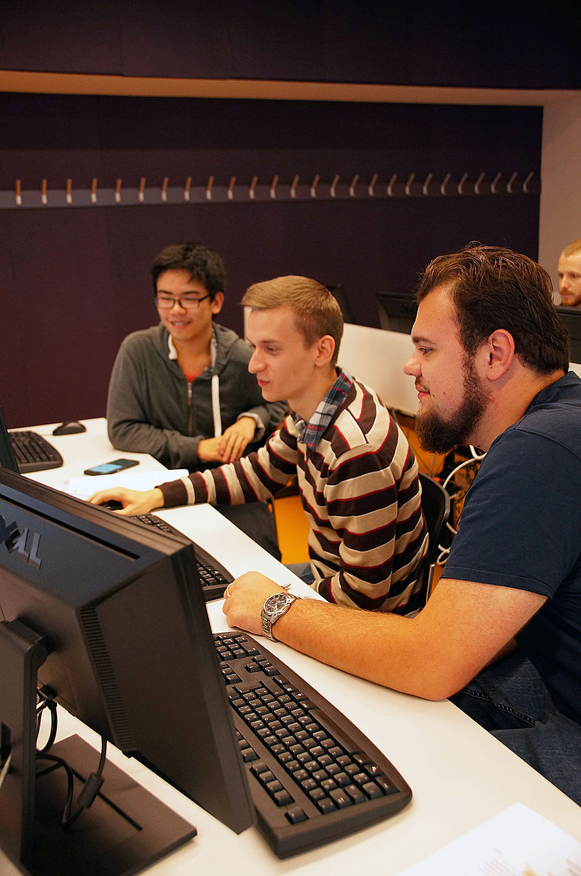 Drei Studierende schauen gemeinsam auf den Bildschirm eines Computers.