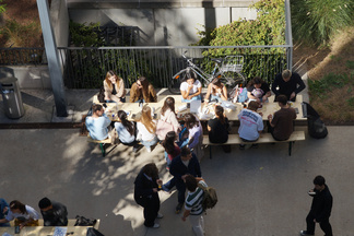Studierende sitzen im Innenhof an einem Tisch zum Essen und Trinken.